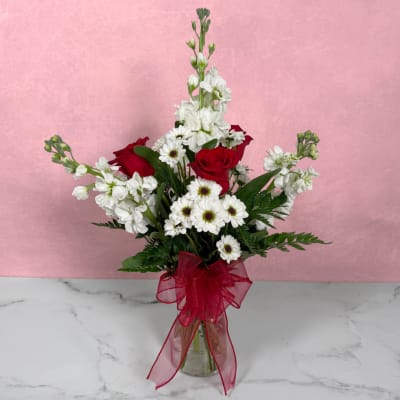 Red roses and white flowers in a clear glass vase with a red ribbon