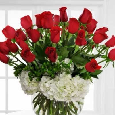 Round vase of red roses arranged above white hydrangeas in a clear glass bowl
