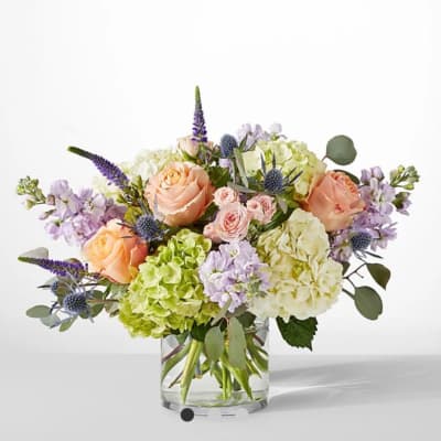 Mixed bouquet of peach roses, hydrangeas, and purple flowers in a glass vase