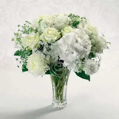 White rose and carnation arrangement in a clear glass vase with silver wire accents