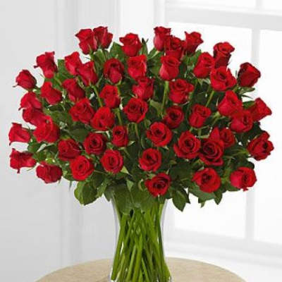 Large bouquet of long-stem red roses arranged in a clear glass vase on a table