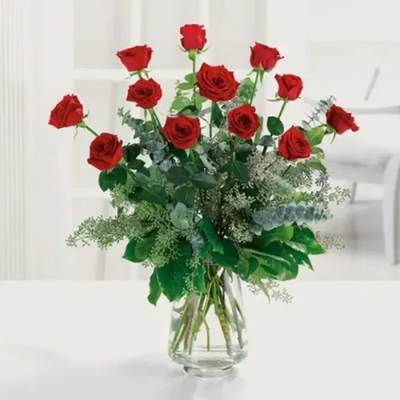 Tall arrangement of long-stem red roses with lush greenery in a clear glass vase