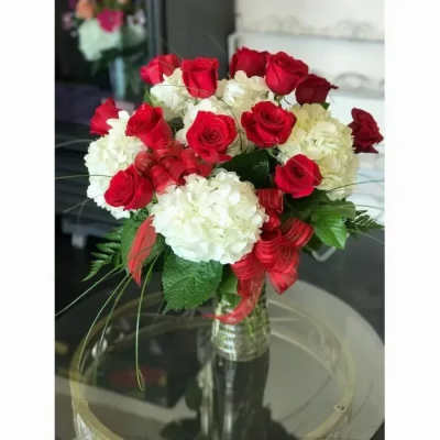 Vase arrangement of red roses and white hydrangeas with red ribbon accents