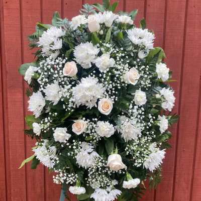 Oval standing spray of white flowers and ivory roses on an easel.