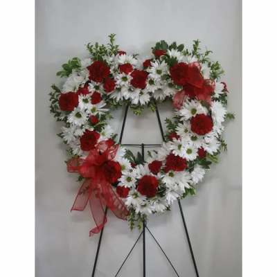 Heart-shaped floral wreath with red and white flowers on a black stand