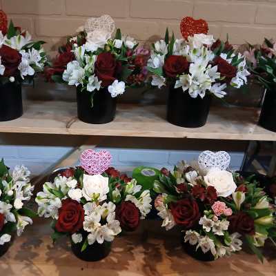 Several red and white floral arrangements in black containers on wooden shelves