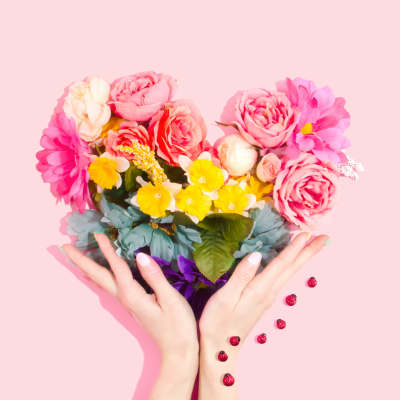 Hands holding a colorful bouquet of pink, yellow, and white flowers