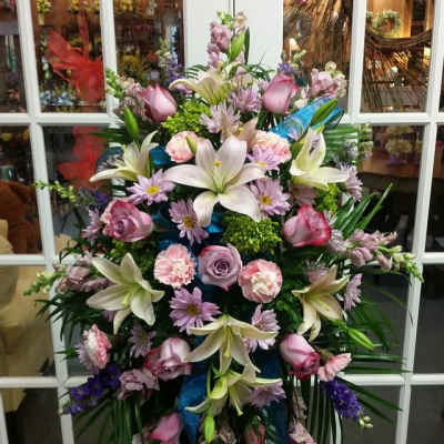 Standing floral spray with lilies, roses, and purple blooms on an easel
