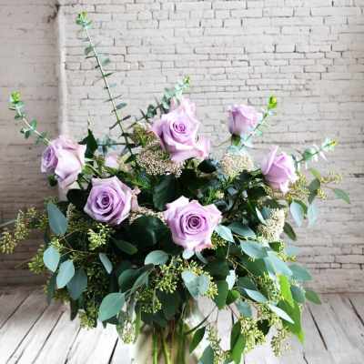 Lavender roses arranged in a glass vase with mixed greenery