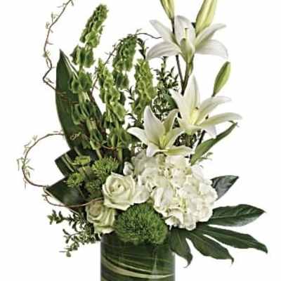 White lilies and hydrangeas in a green glass vase with foliage