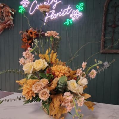Autumn floral arrangement with cream roses, peach blooms, and orange flowers in a vase