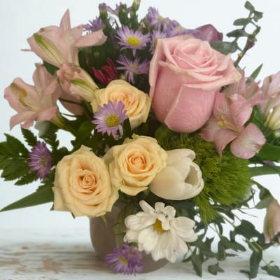 Pink and cream bouquet with roses, lilies, and purple daisies in a vase