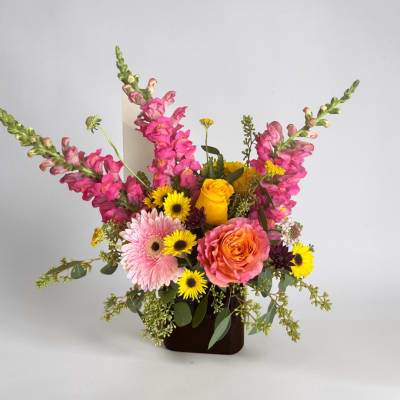 Mixed bouquet with pink snapdragons, roses, gerbera daisies, and yellow daisies in a dark vase