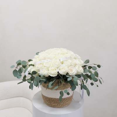 White rose arrangement in a woven basket with eucalyptus