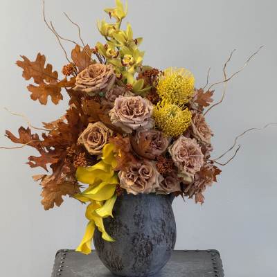 Autumn floral arrangement in a dark vase with yellow orchids and roses