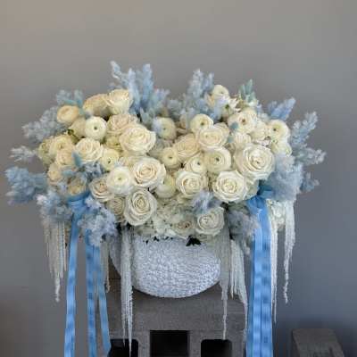 Large white rose arrangement with pale blue accents in a textured vase
