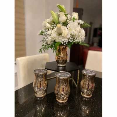 White floral arrangement in a gold vase with three matching votive holders