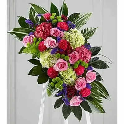 Standing floral spray with pink roses and mixed blooms on a white easel