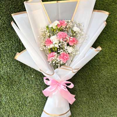 Pink and white carnation bouquet wrapped in white paper with a pink ribbon