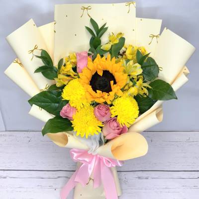 Bouquet of yellow sunflowers, pink roses, and yellow mums wrapped in cream paper