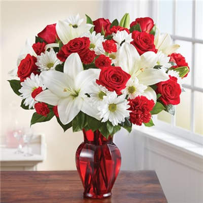 Red roses and white lilies with daisies in a red glass vase