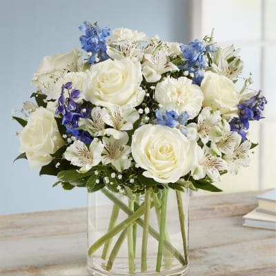 White roses and blue flowers arranged in a clear glass vase