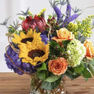 Mixed bouquet with sunflowers, roses, hydrangea, and purple spikes in a glass vase