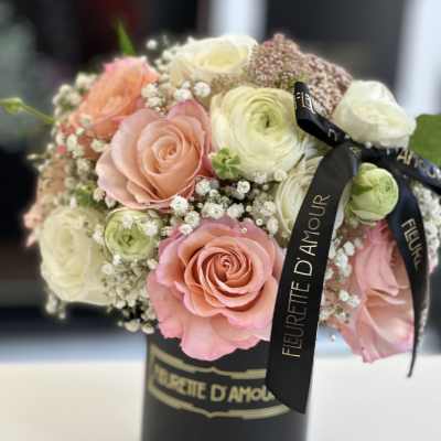Pink and white roses arranged in a black hatbox with ribbon