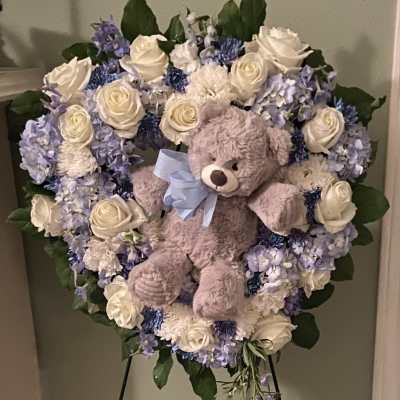Heart-shaped floral wreath with a teddy bear and blue ribbon on an easel
