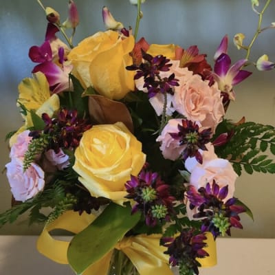 Bouquet of yellow and pink roses in a glass vase with a yellow ribbon