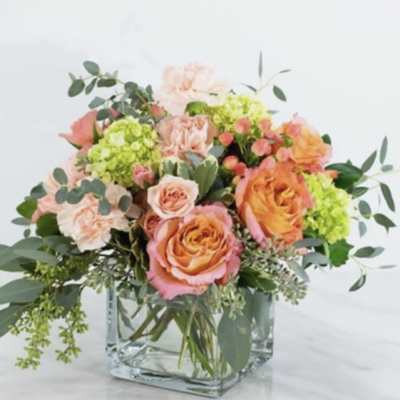 Peach and coral roses in a clear glass vase with green filler flowers
