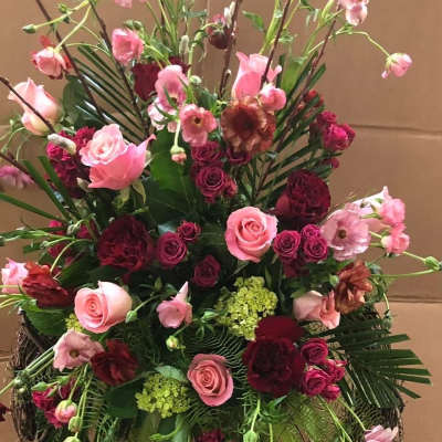 Large pink and burgundy floral arrangement in a wicker stand