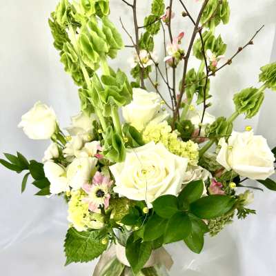 White roses and pink blossoms in a glass vase with tall green stems