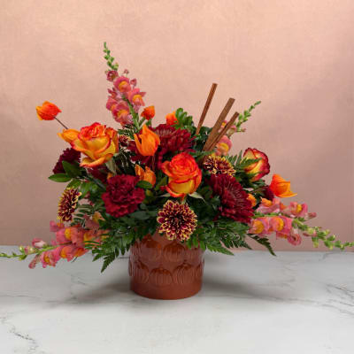 Mixed orange, pink, and burgundy flowers in a brown vase