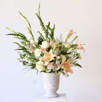 Peach lilies and white roses in a white pedestal vase