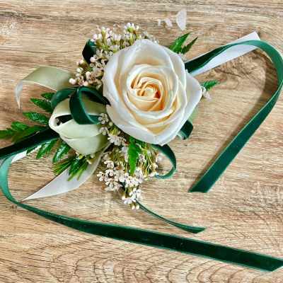 White rose corsage with green and ivory ribbons on a wooden surface