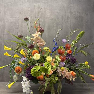 Large mixed floral arrangement with orchids, calla lilies, and bright accent blooms