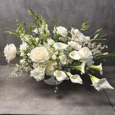White floral arrangement with roses, calla lilies, and orchids in a low vase