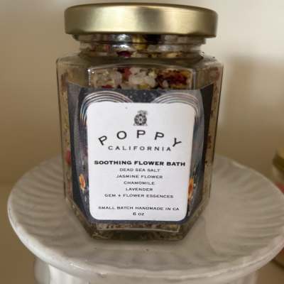 Jar of flower bath salts with a gold lid on a white pedestal
