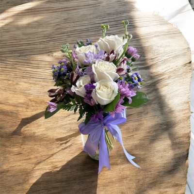 Small vase arrangement of white roses and purple flowers with a lavender ribbon bow