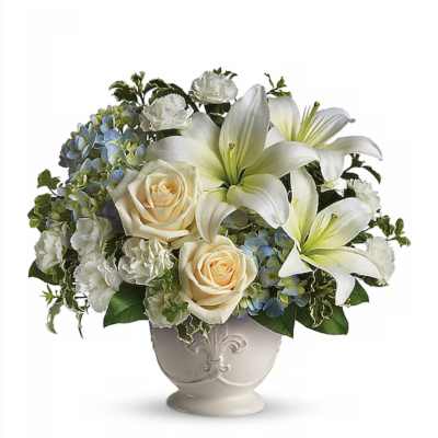 White lilies, cream roses, and blue hydrangeas arranged in a white ceramic urn-style vase