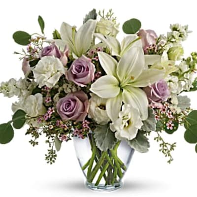 Pastel bouquet of white lilies and lavender roses arranged in a clear glass vase