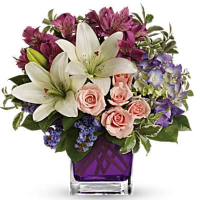 Bouquet of white lilies, pink roses, and purple flowers in a purple vase