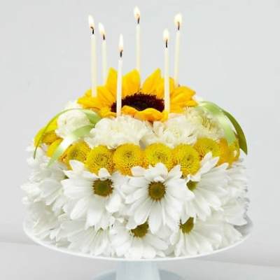 Sunflower and daisy cake with lit candles on a pedestal stand