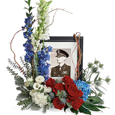 Floral tribute around a framed military portrait with red, white, and blue flowers