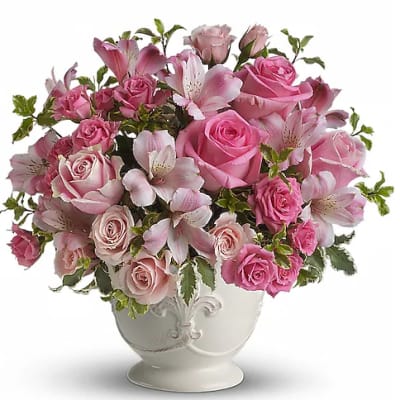 Pink roses and lilies arranged in a white urn vase