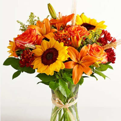 Bouquet of sunflowers, orange lilies, and roses in a clear glass vase