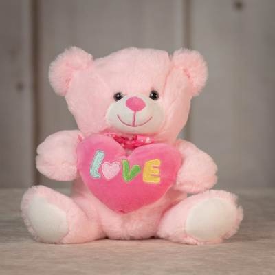 Pink teddy bear holding a pink heart pillow with the word love