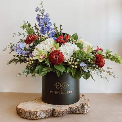 Mixed floral arrangement in a black hatbox with red, white, blue, and green blooms