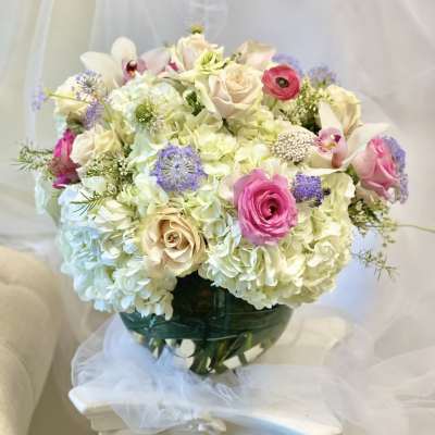 Bouquet of pale hydrangeas, pink roses, and white orchids in a glass vase